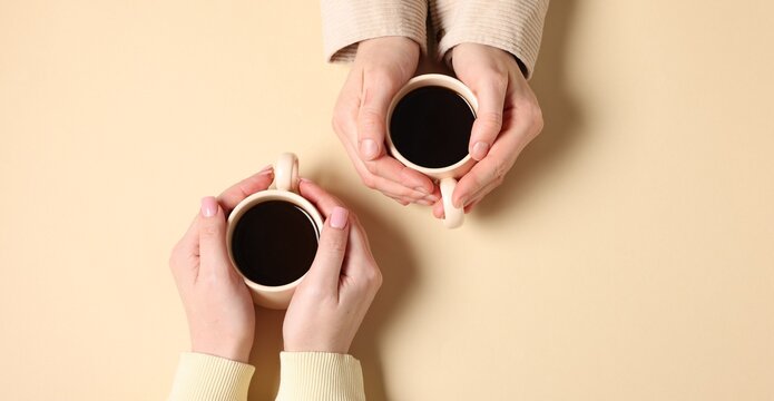 Friends with cups of aromatic coffee on beige background, top view