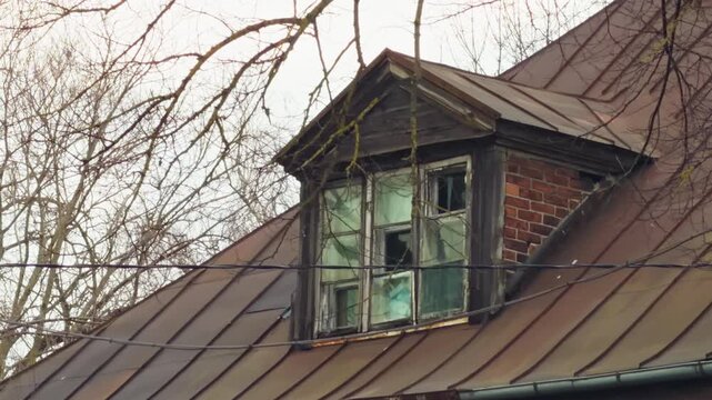 Decayed rural building details. Old dormer with peeling paint and moss growth