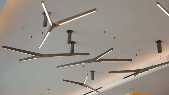 Metal lights hang in soft space, warm glow falls on clean ceiling, sharp lines form calm modern look. Gentle shine and simple shapes create quiet bright room.