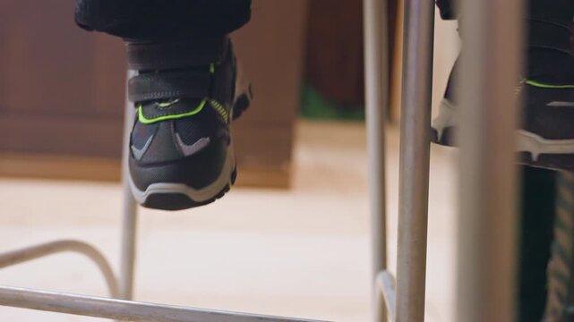 Small sneakers dangling under kitchen counter, young son sits on high stool while mother prepares meal, closeup of black shoes with neon green accents, gentle warm light, quiet domestic waiting, soft