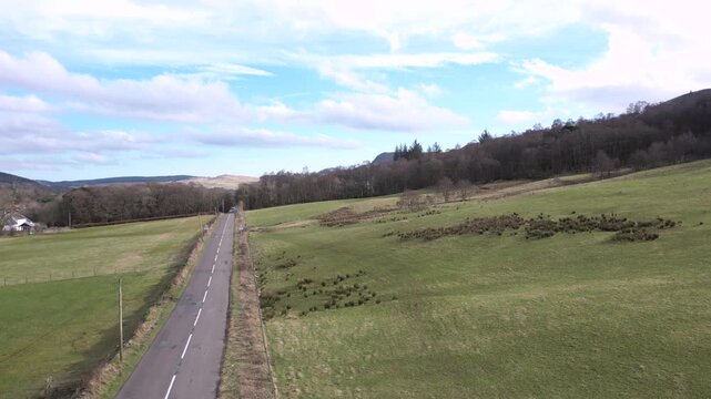 A low level ascent to reveal the main street of a picturesque rural village in Central Scotland nestled in a valley below the Campsie Hills. No road signs or location markers.

