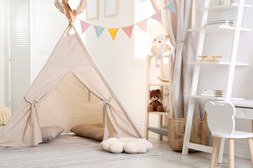 Stylish toy wigwam, furniture, pillows and decor in light playroom. Interior design © New Africa