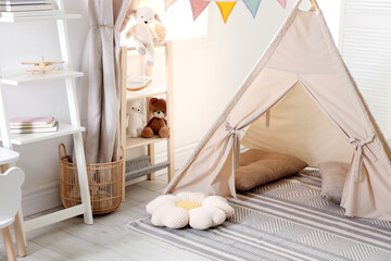 Stylish toy wigwam, furniture, pillows and decor in light playroom. Interior design © New Africa