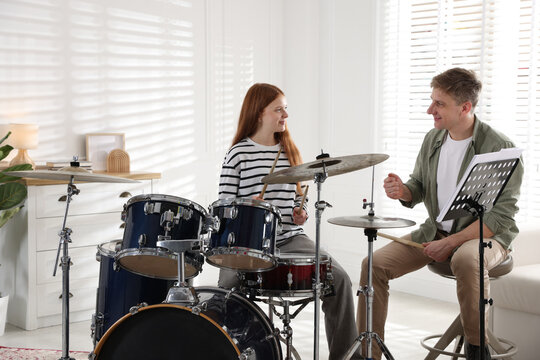 Teenage girl learning how to play drums with music teacher indoors