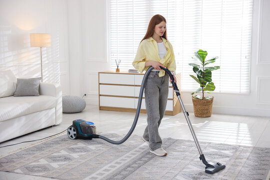 Teenage girl cleaning carpet with vacuum cleaner at home