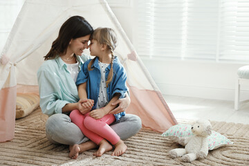 Mother and her daughter near toy wigwam at home, space for text © New Africa