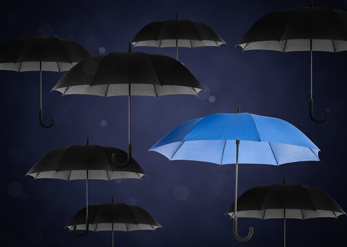 Blue umbrella among black ones against dark background