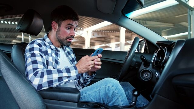 Happy young man reading message on the smartphone while sitting in the car. Transport, technology, lifestyle concept.