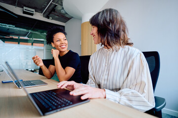 Diverse businesswomen working and smiling together, discussing ideas during a professional corporate meeting in a modern office space