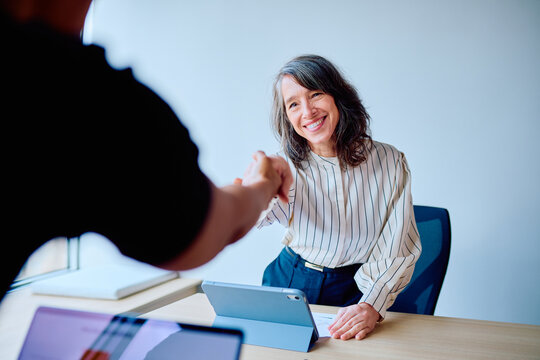 Mature businesswoman smiling while shaking hands with a partner, completing a professional meeting or interview in an office