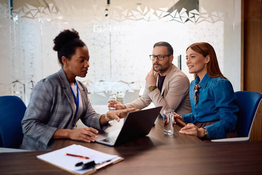 Black financial advisor using laptop while talking to couple on meeting in office.