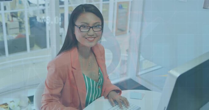 A young female business creative is working in a modern office, using a computer and smil
