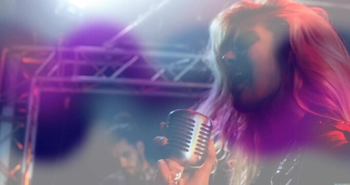 Female singer grabbing mic and singing for performance, guitarist strumming under lens flares