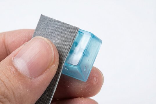 Hand holding a small square of sandpaper to wet sand the edges of a custom translucent blue resin keyboard keycap
