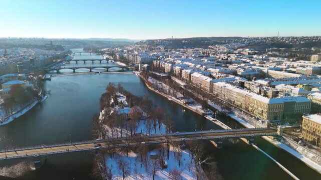 Aerial view of snowy Prague, Czech Republic. Winter cityscape with Snow-covered rooftops, Vltava River, and sunny blue sky
