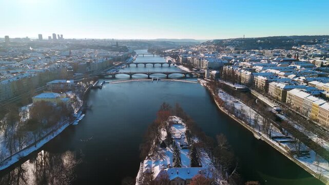 Aerial view of snowy Prague, Czech Republic. Winter cityscape with Snow-covered rooftops, Vltava River, and sunny blue sky