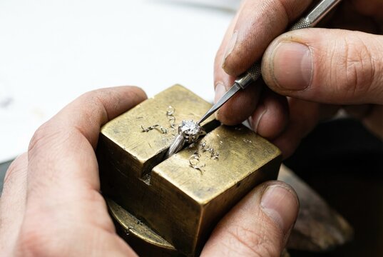 Jeweler making a diamond ring by pushing metal prongs over the stone with a graver
