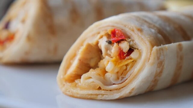 Close up slow motion video of chicken fajita tortilla wrap with fresh vegetables on white plate.