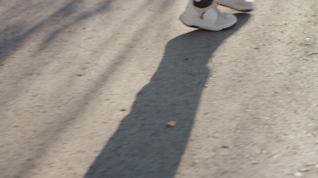 Closeup shadows and sneakers on pavement long silhouette stretched across asphalt slow idle step paired shoes reflective light moody cinematic frame suspicious mood potential prowler tension in quiet