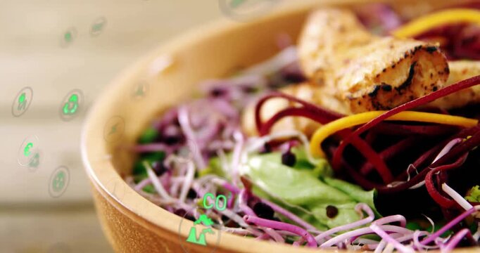 Moving camera revealing wood bowl on rustic table focusing on greens, grilled piece and eco icons