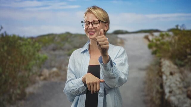 Woman pointing with index finger then giving a thumbs up, hand visible on a rural street with stonewall and bushes; encouragement cheerful.