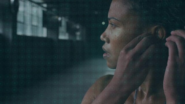 Female athlete finishing set and pausing in gym, adjusting wired earbud, securing cord, refocusing