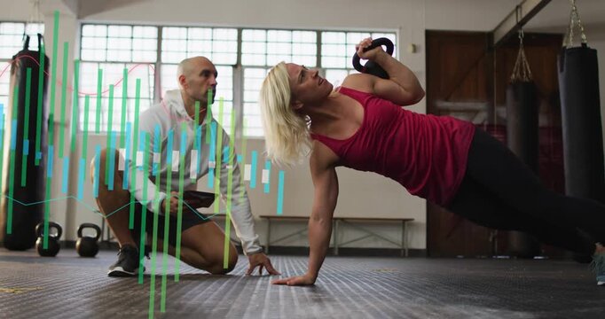 Trainer cueing tablet, woman in red tank top rotating, pressing kettlebell up at gym for balance
