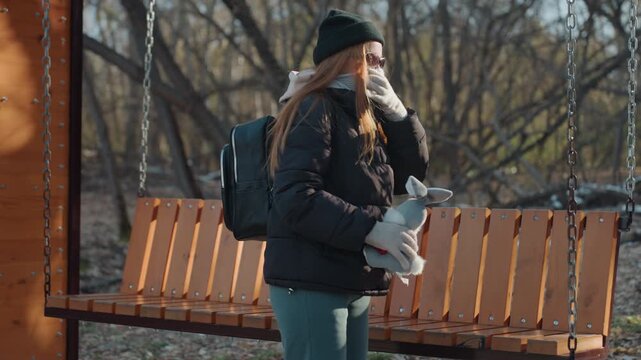White snatcher returns plush rabbit to wooden swing bench, remorseful walk through snowy park as sunlight and shadows soften scene backpacked passerby places toy back, pause of regret and quiet