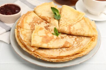 Tasty crepes with mint leaves and jam served on white tiled table, closeup © New Africa
