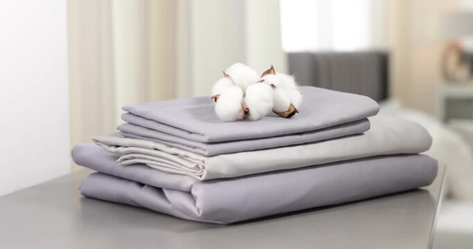 Stack of fresh bed linens and cotton flowers on grey chest of drawers indoors, closeup. Camera moving forward