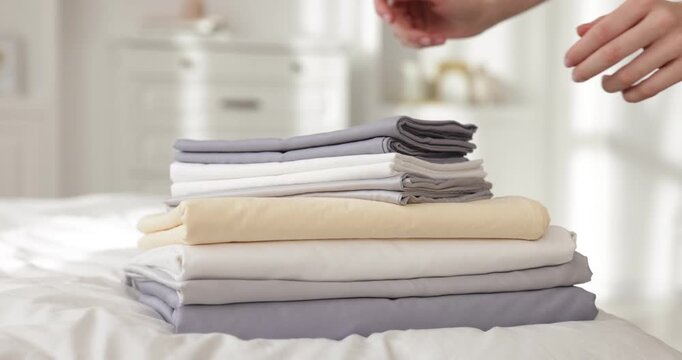 Woman putting stack of fresh linens onto bed indoors, closeup