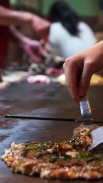 Chef flipping authentic okonomiyaki on a teppan grill in Osaka, Japan