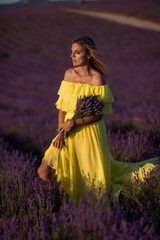 Obraz premium Woman lavender field beautiful blonde model in flowing yellow dress holding flowers at sunset