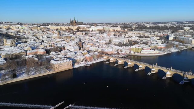 Aerial view of snowy Prague, Czech Republic. Winter cityscape with Charles Bridge, Vltava River, and Prague Castle (Hradcany). Clear blue sky. Sunny historic European landmark