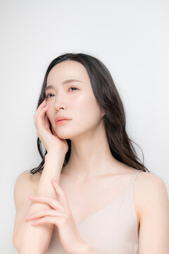 黒髪のパーマのロングヘアで白背景の若い女性のビューティーイメージ　スキンケアなどのツヤ肌、保湿や高級感のあるラグジュアリーな美容イメージアンニュイな表情