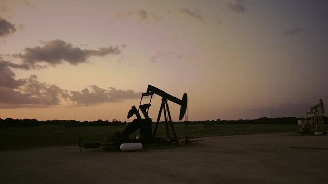 Silhouette of Oil Pump Jack in Rural Field Under Vibrant Twilight Sky.