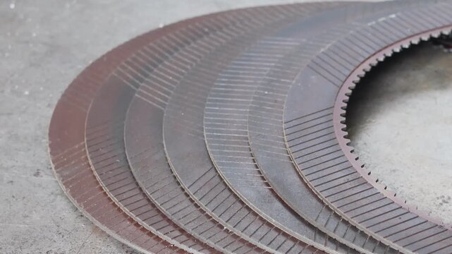Close-up panning shot of a stack of new, metallic friction clutch plates on a workshop floor, showing complex internal and external spline teeth.