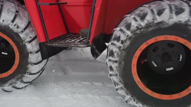 Red atv rider winter snow offroad red quad navigating snowy forest trail, closeup tire shots show heavy tread packed with snow, rider in camouflage gear steers uphill across frozen field, overcast sky