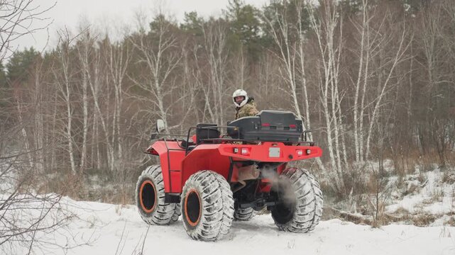 Red atv tearing through snowy forest, rider navigating icy track, tires digging into snow, exhaust vapor rising, overcast birch backdrop, high adrenaline offroad action and tight turns