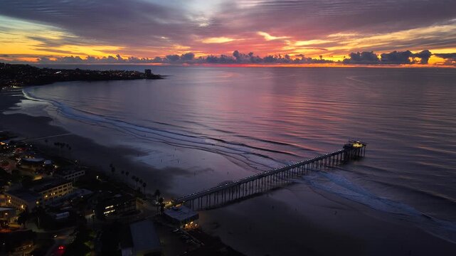Aerial video footage of a ocean pier with sunning sunset skies and streets and neighborhood view in foreground in blue hour, car and street lights light up the scena.  