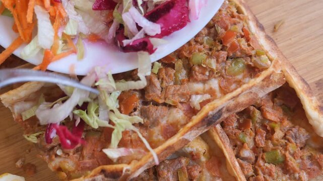 Serving traditional Turkish flatbread pide with fresh salad topping on wooden board.