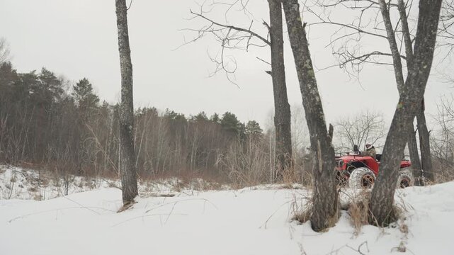 Red atv climbing snowy bank closeup machine focus on heavy tread and chains rider controlling throttle intense motion through birch lined field overcast sky raw power traction emphasized adrenaline