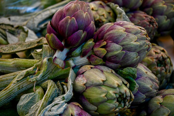 Fototapeta premium Stack of purple and green artichokes at market