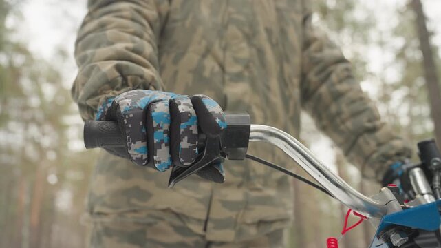 Closeup gloved hand on atv throttle in pine forest practices precise control and balance, camo jacket and helmet in soft winter light, handlebar and LED light visible, repeated grip adjustments show