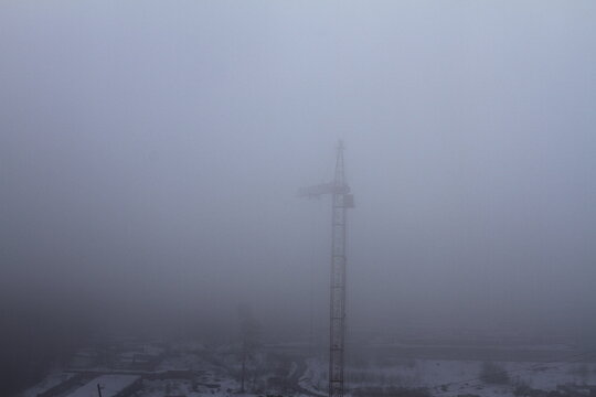 Thick fog at the construction site. Poor visibility prevents the tower crane from working.