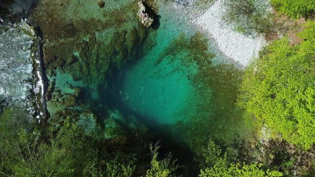 Aerial top view of turquoise spring water surrounded by lush green forest, Oko Skakavice in Montenegro, 4k