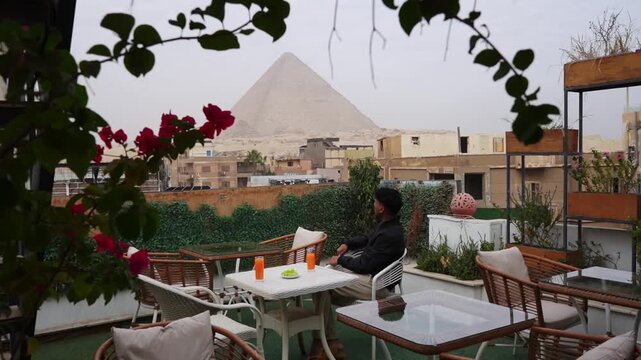 Man sitting at rooftop terrace with pyramid view in Egypt