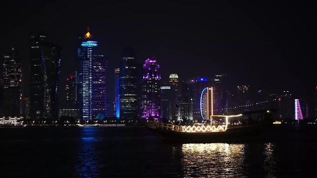 Traditional dhow boat sailing in front of Doha skyline at night, Qatar