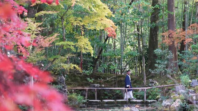 Man in kimono standing on bridge in Japanese autumn garden