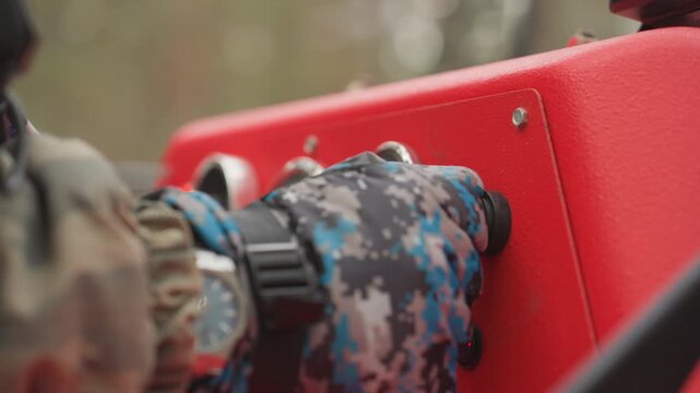 Red control panel with gauges, gloved hand turns ignition knob with keyhole nearby, closeup reveals dials, wiring and mounting bolts on painted metal, operator inspection before drive, utility vehicle